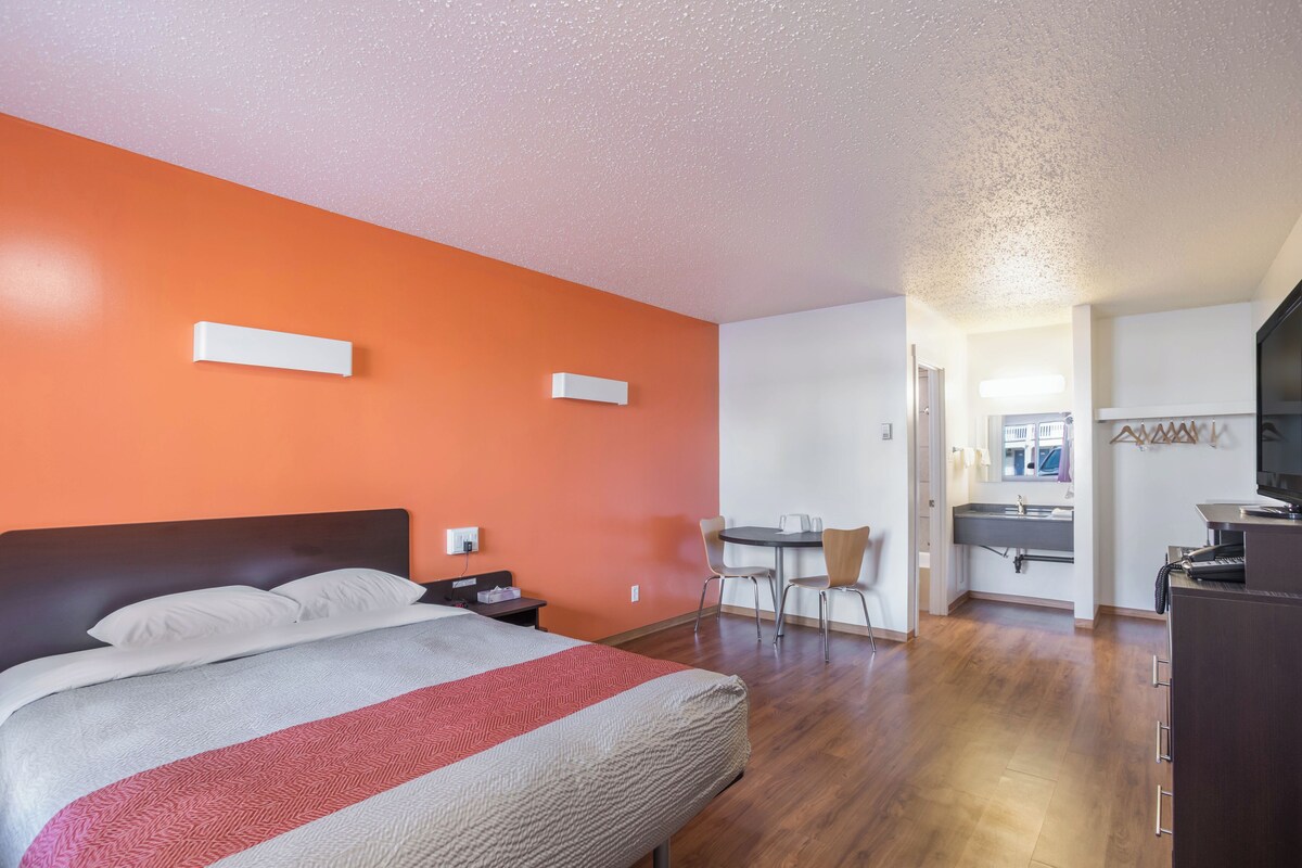 A hotel room with a bed, a desk, a chair, a small table, and a kitchenette area.
