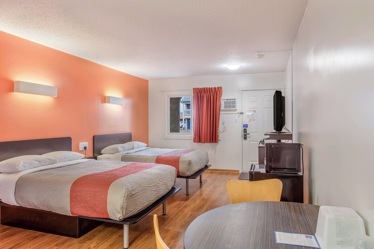 A hotel room with two beds, a dining table, a TV, and a window with curtains.