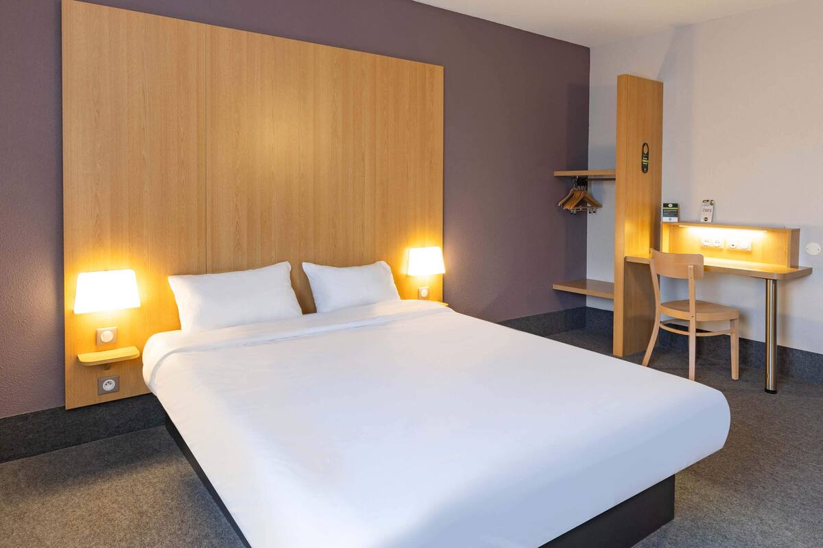 Ein Hotelzimmer mit einem großen Bett, zwei Nachttischlampen, einem Schreibtisch mit Stuhl und einem Holz-Kopfteil.