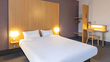 A hotel room with a large bed, two bedside lamps, a desk with a chair, and a wooden headboard.