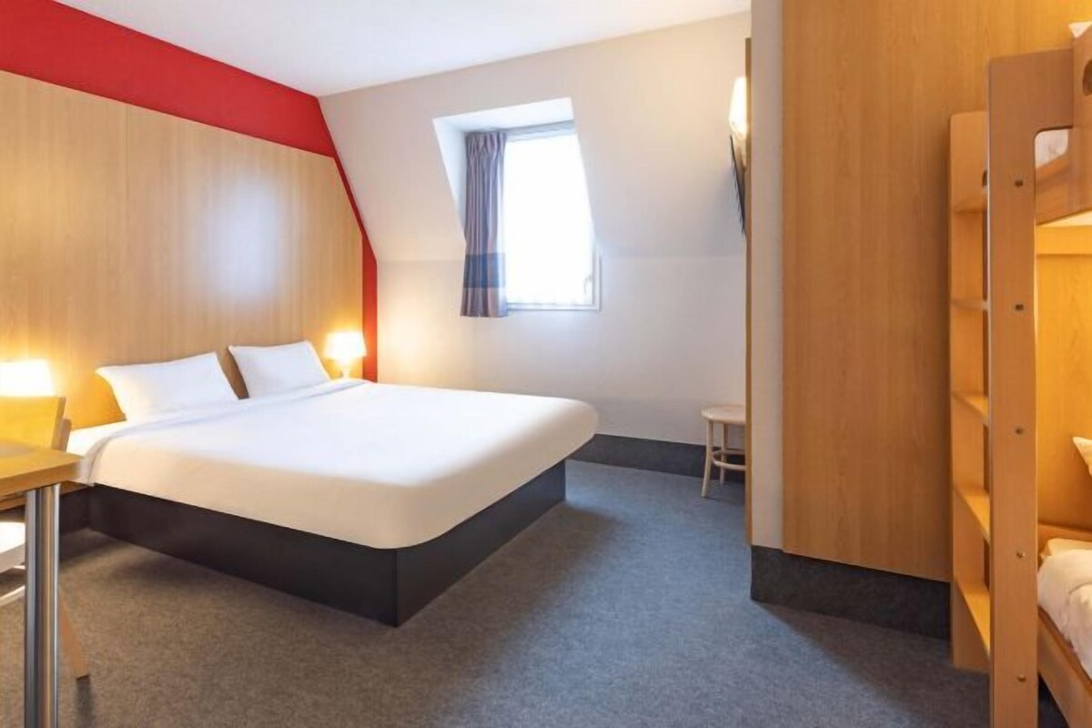A hotel room with a bed, a desk, a chair, and a window with curtains.