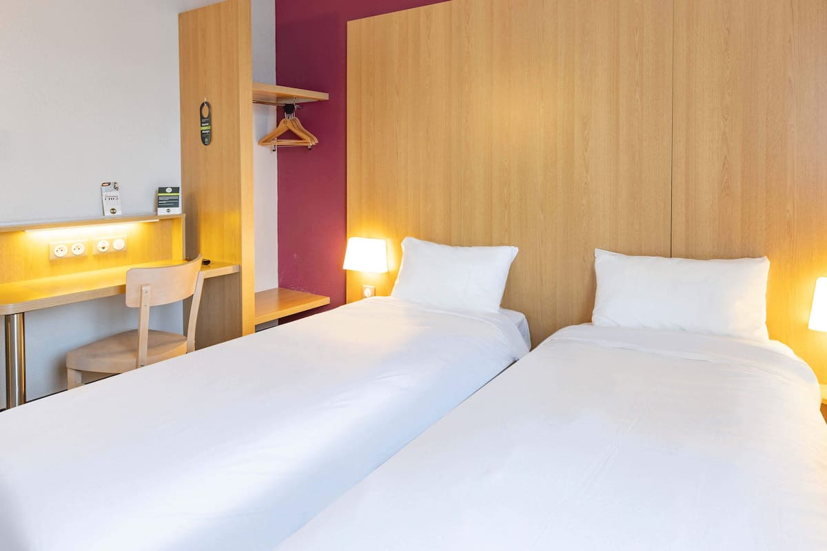 Ein Hotelzimmer mit zwei Betten, einem Schreibtisch, einem Stuhl und einem Holzschrank.