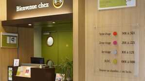 A hotel reception desk with a sign reading "Bienvenue chez B&B Hotels" and a directory with room numbers.