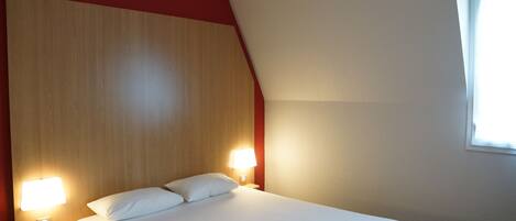 Habitación de hotel con una cama grande, dos lámparas de noche, un cabecero de madera y una ventana con luz diurna.