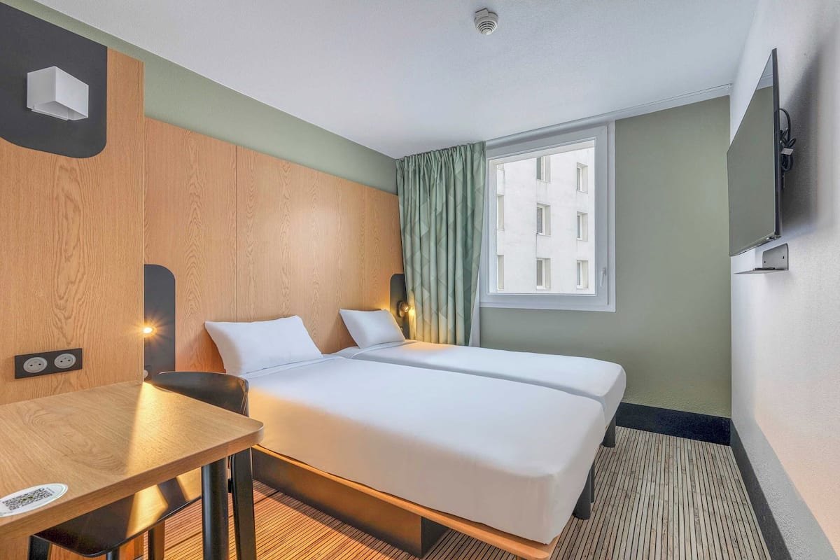 Une chambre d’hôtel avec un lit, un bureau, une chaise, une télévision et une fenêtre avec des rideaux.