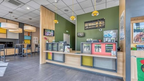 Una zona de recepción moderna con mostrador de madera, luces colgantes amarillas y pared verde.