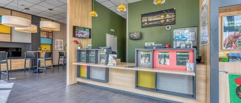 A modern reception area with a wooden counter, yellow pendant lights, and a green wall.