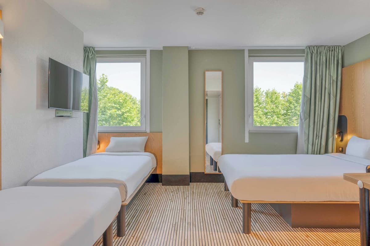 Une chambre d’hôtel avec deux lits, un téléviseur à écran plat, un miroir et de grandes fenêtres avec des rideaux.