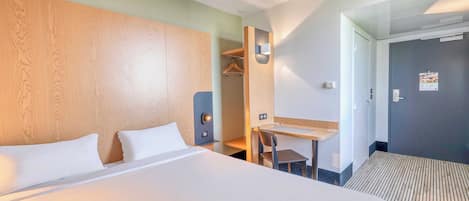 A hotel room with a large bed, a desk, a chair, a wardrobe, and a door.