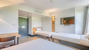 Una habitación de hotel con una cama grande, dos camas individuales, un escritorio y un televisor.