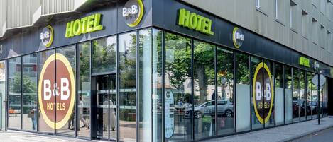 Un moderno hotel tipo B&B con fachada de vidrio, ventanas amplias y un logotipo circular destacado.