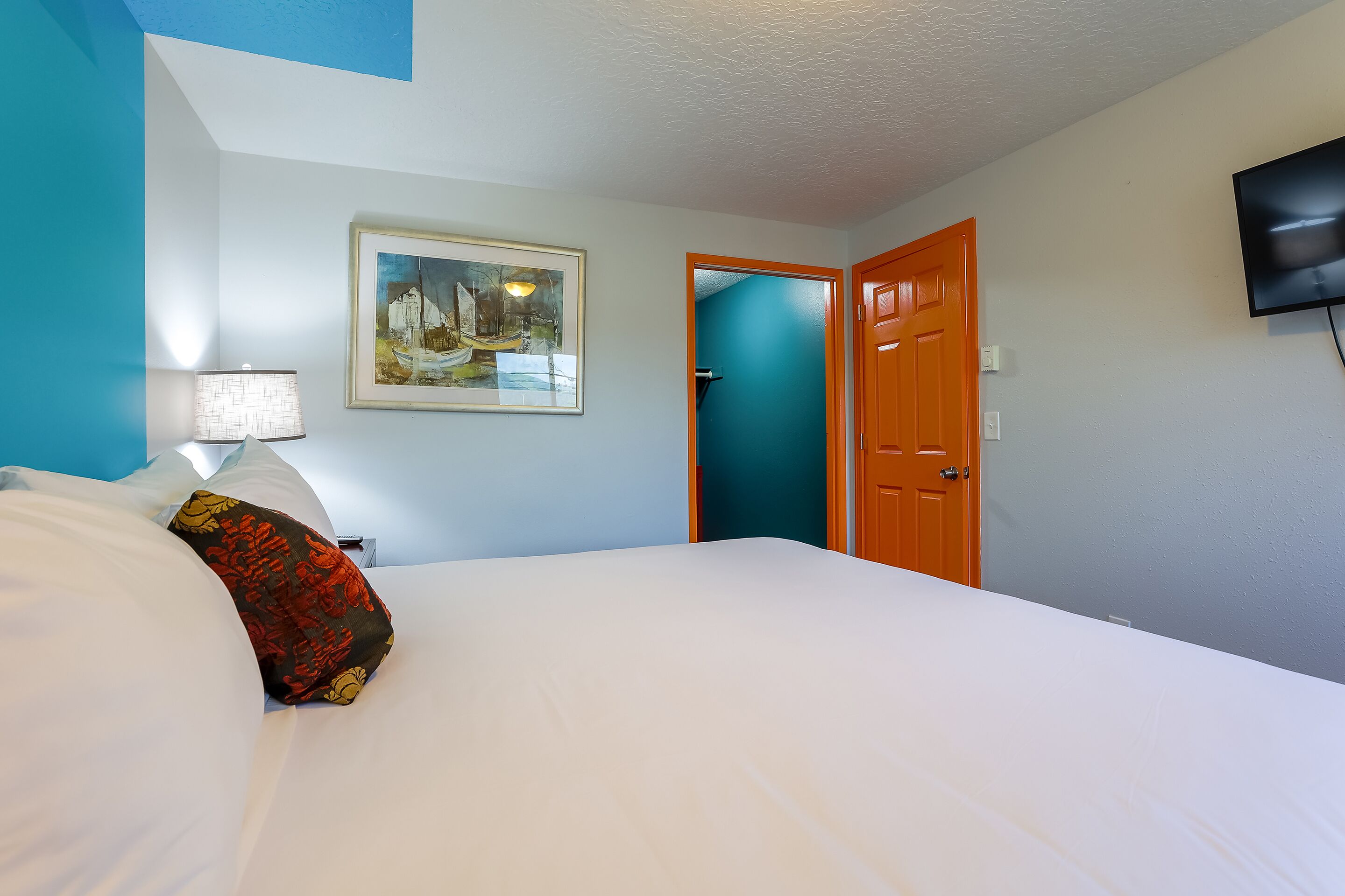 A hotel room with a bed, a painting on the wall, a television, and a door.