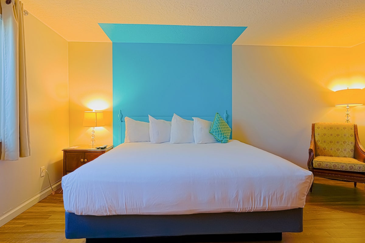 A hotel room with a large bed, two bedside lamps, a chair, and a blue accent wall.