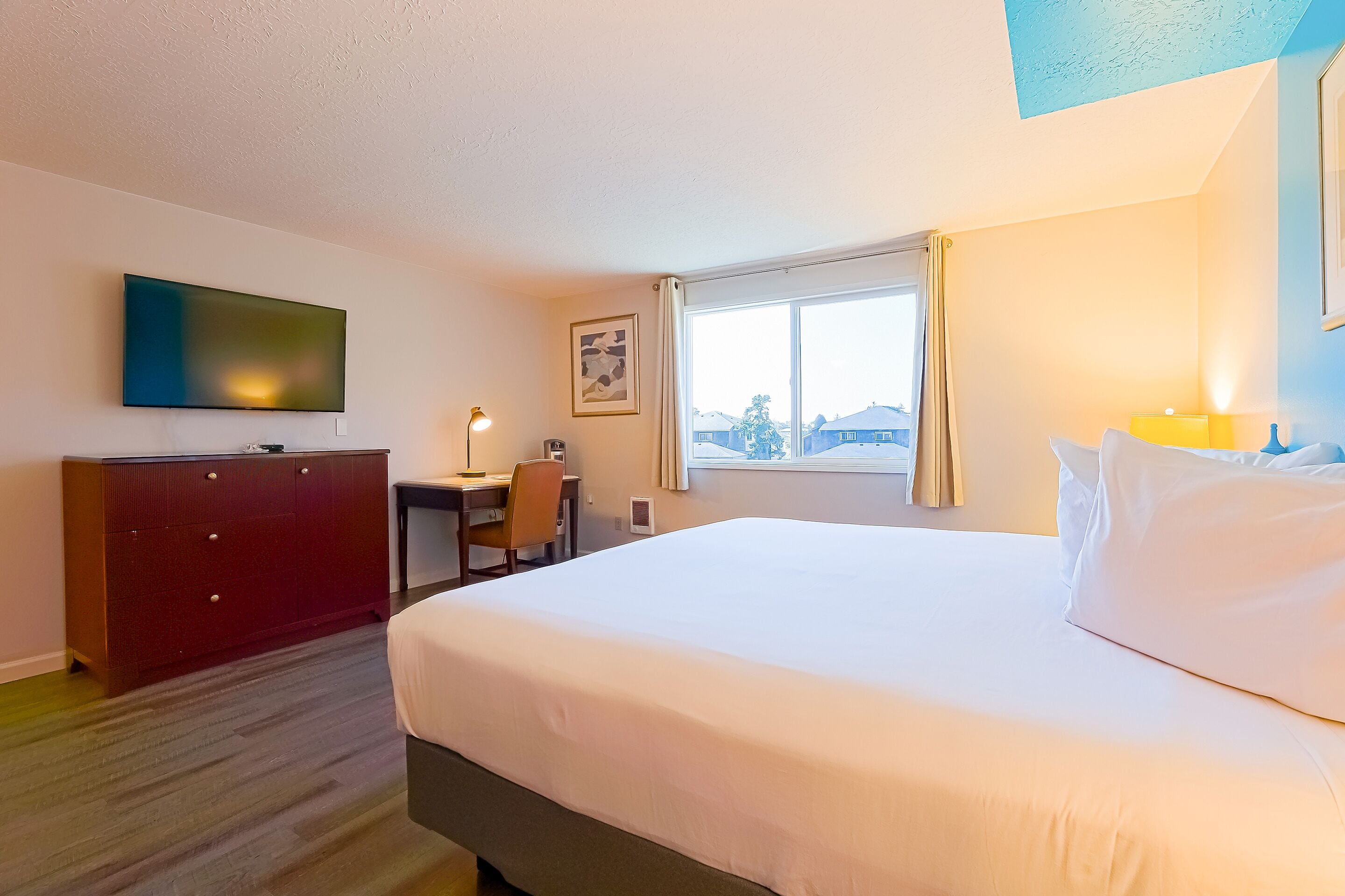 A hotel room with a large bed, a desk, a chair, a TV, and a window with curtains.