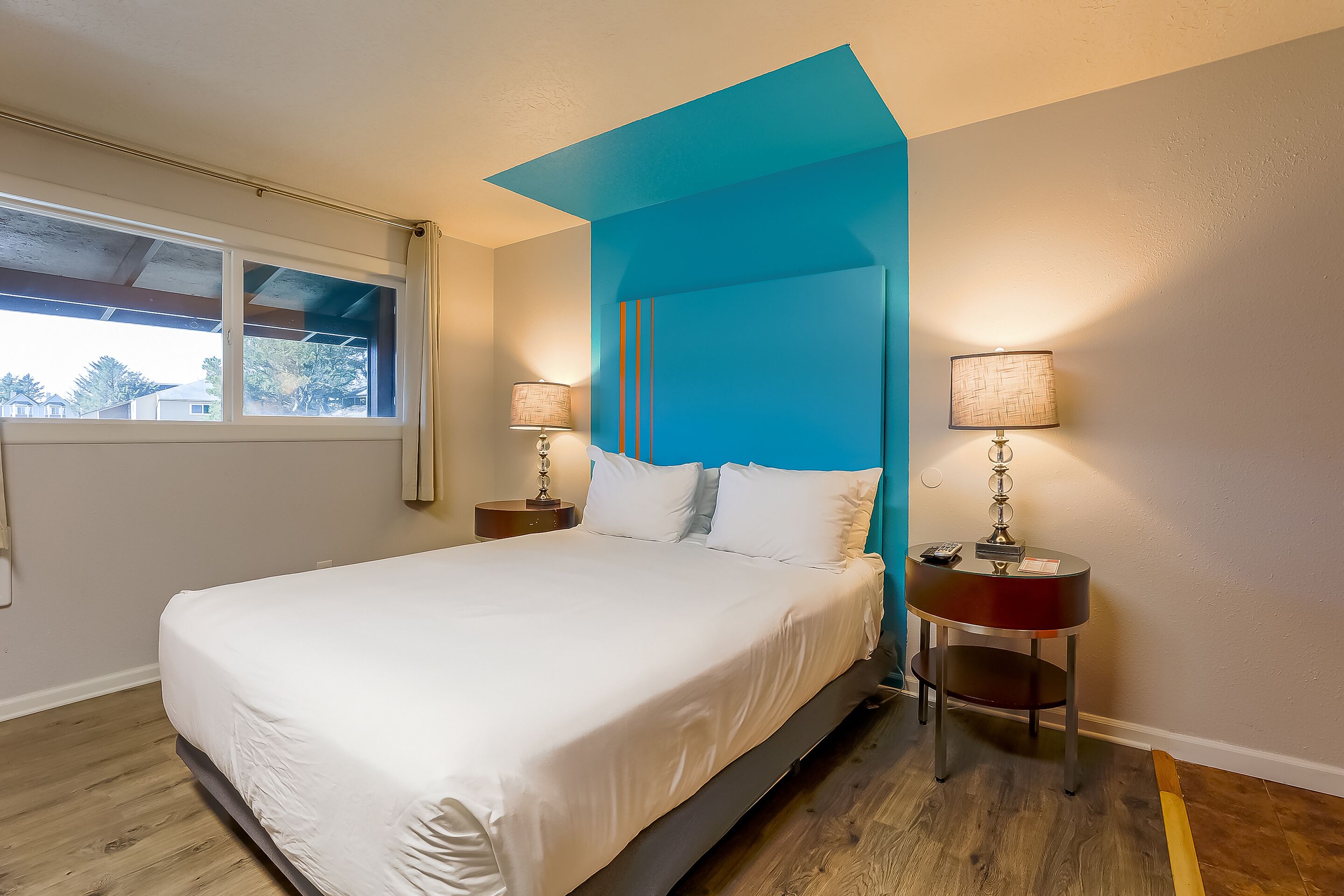 Un dormitorio moderno con una cama grande, dos mesitas de noche con lámparas y un ventanal con vistas a casas.