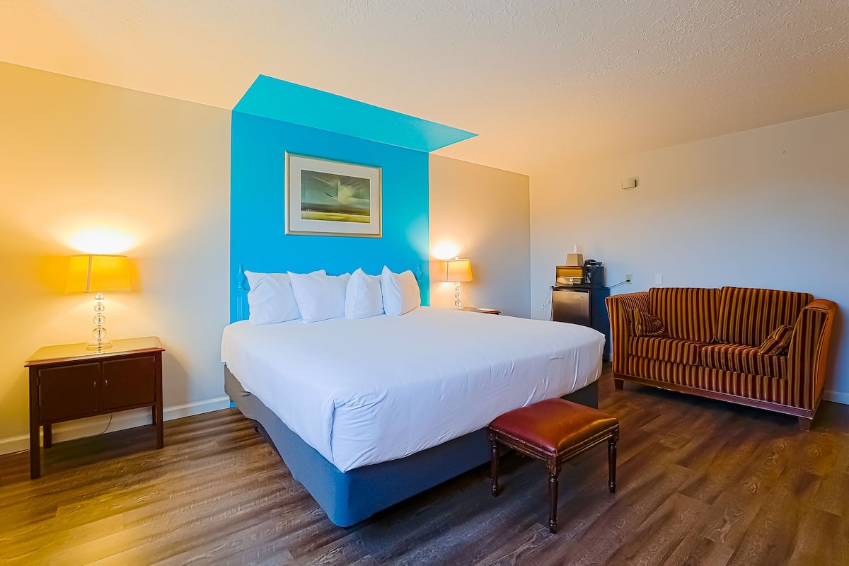 A hotel room with a large bed, two bedside lamps, a sofa, and a wooden floor.