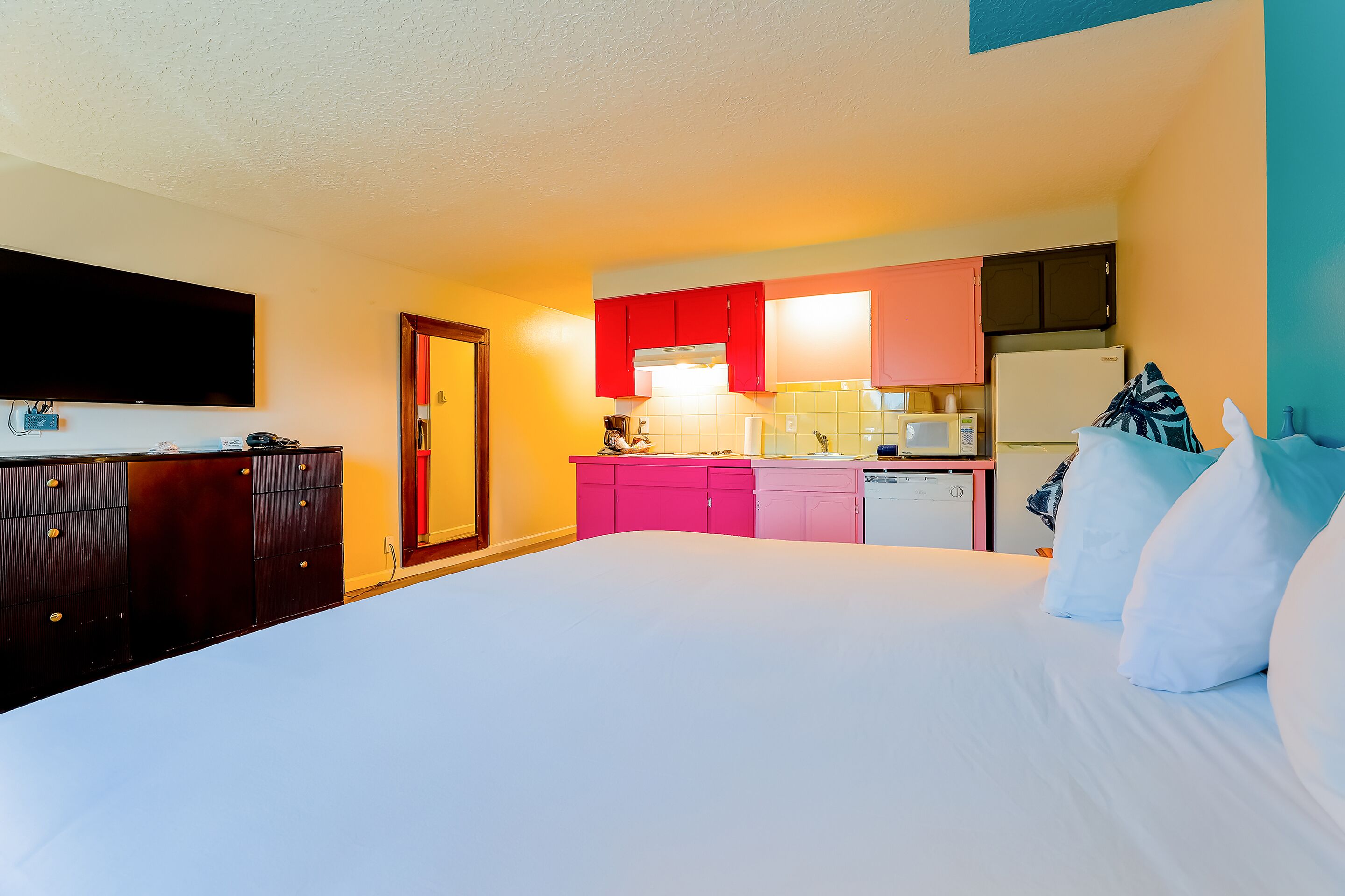 Una habitación de hotel con cama, televisión, kitchenette y baño.