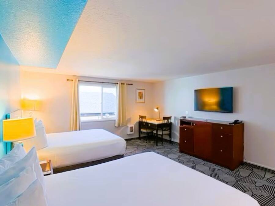 Ett hotellrum med två sängar, ett skrivbord, en stol, en garderob och en tv på väggen.