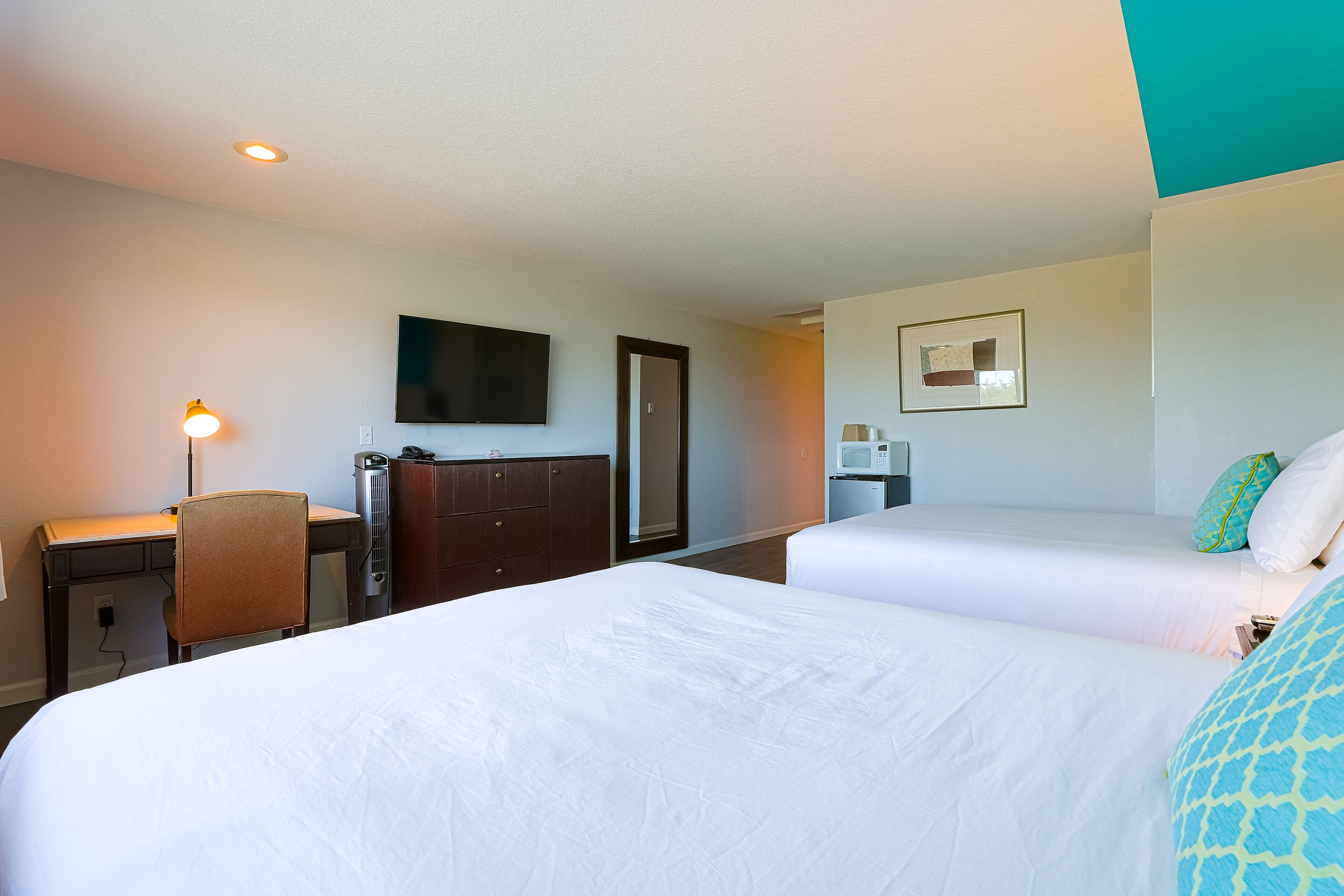 Une chambre d’hôtel avec deux lits, un bureau, une chaise, une télévision et un miroir.