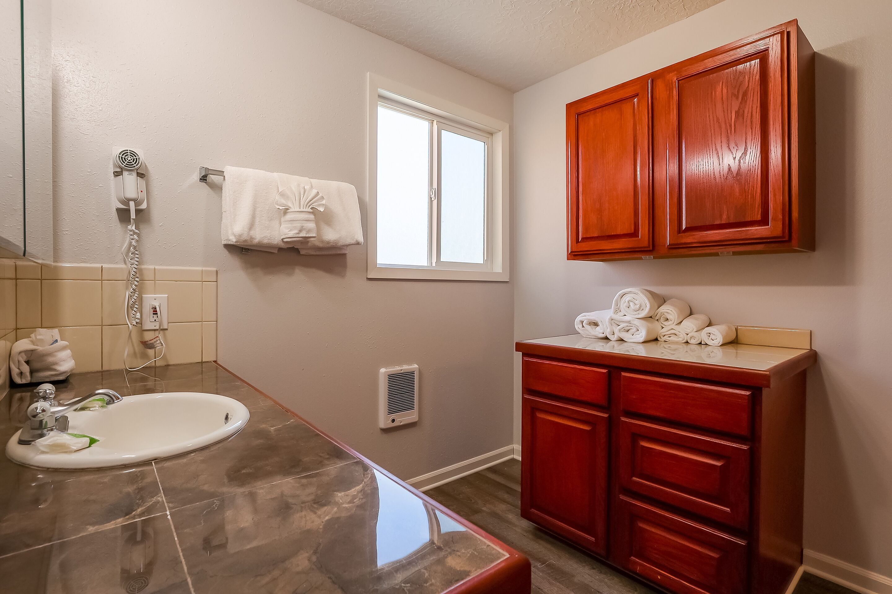 A bathroom with a sink, a towel rack, a window, and wooden cabinets.