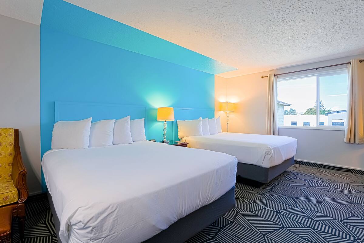 A hotel room with two beds, a large window, and a patterned floor.