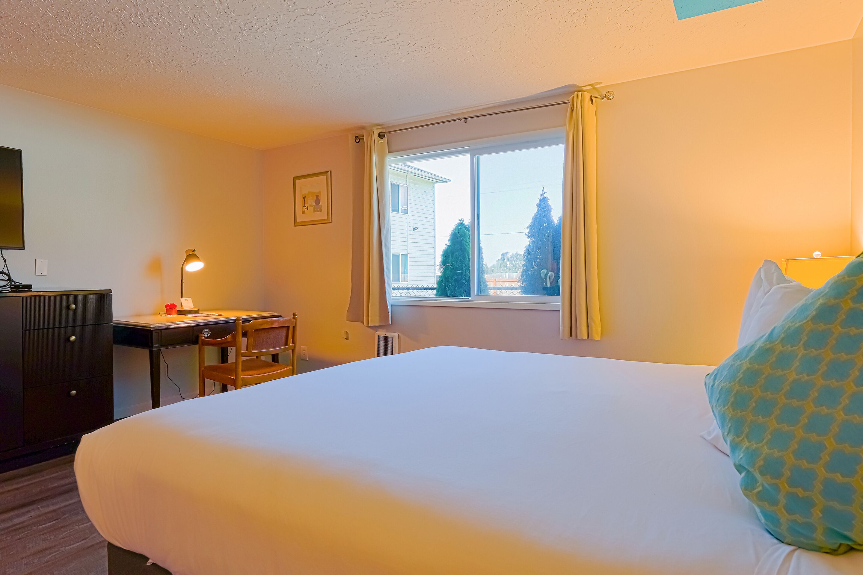 Una habitación de hotel con una cama grande, un escritorio con lámpara, una silla y una ventana con cortinas.