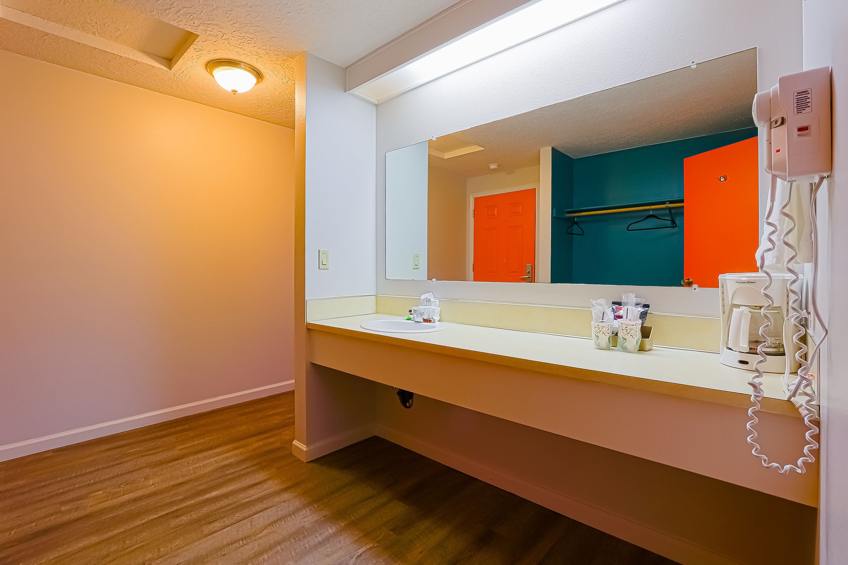 Un baño con lavamanos blanco, espejo, secador de pelo y cafetera.