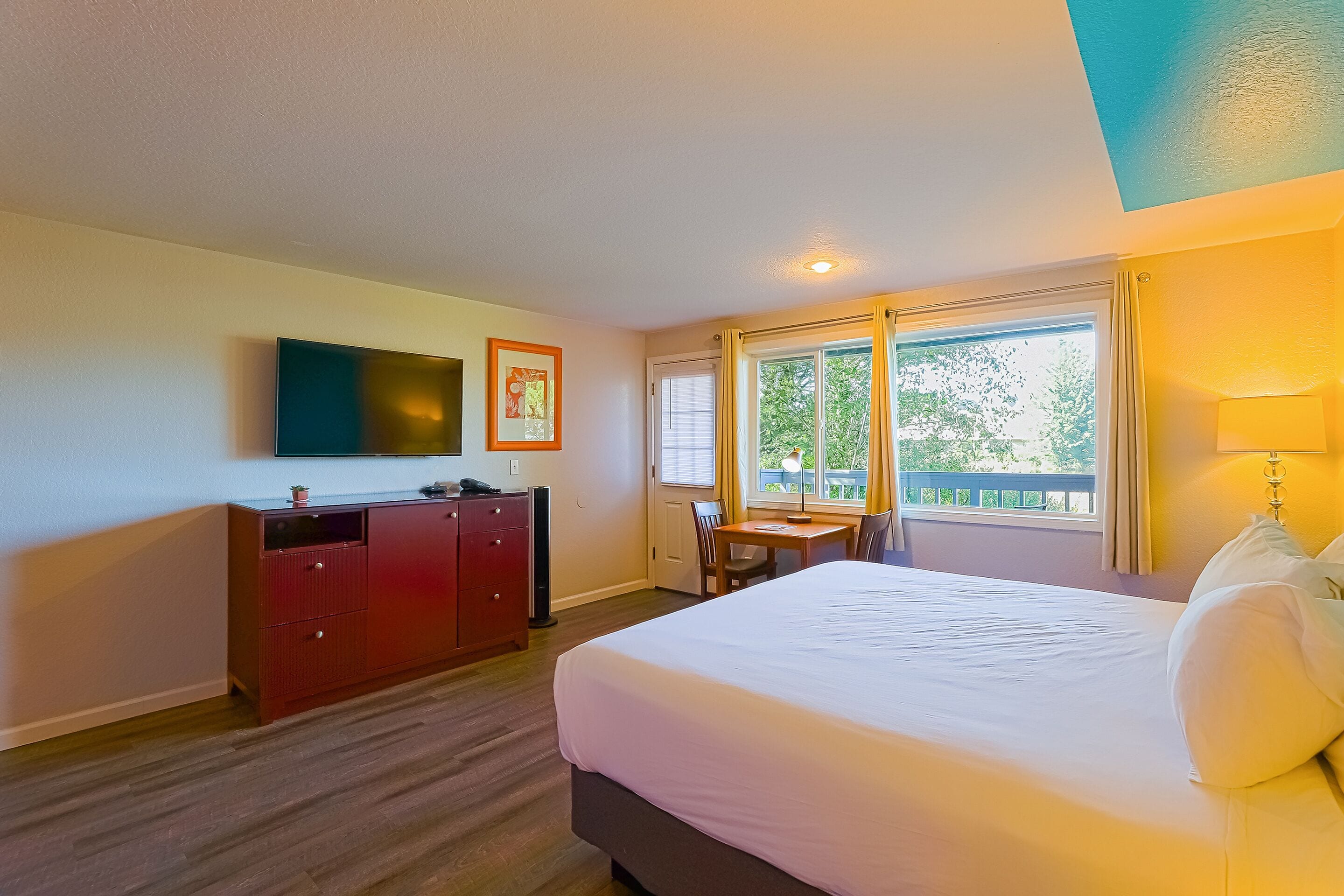 A hotel room with a bed, a desk, a TV, and a window with curtains.
