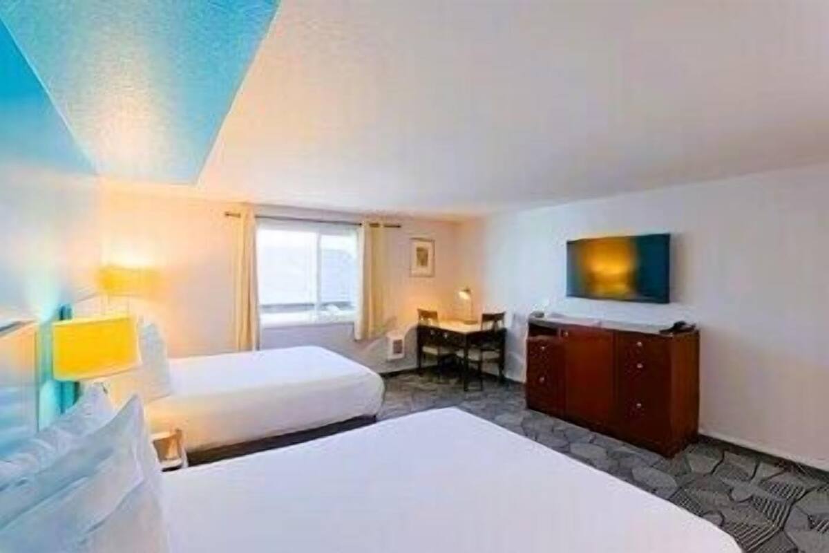 A hotel room with two beds, a desk, a television, and a window.
