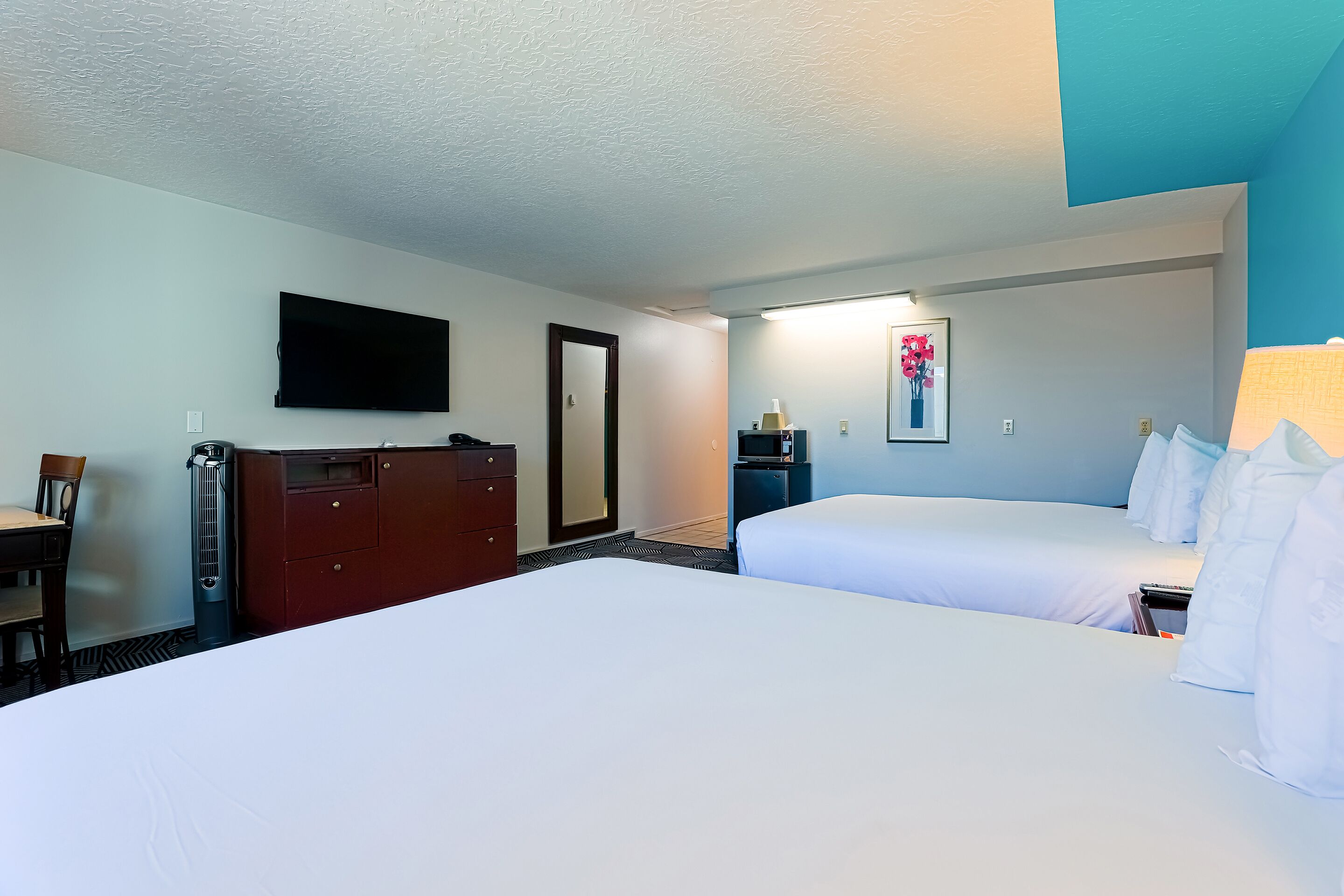 Habitación de hotel con dos camas, un televisor montado en la pared, un escritorio con una silla y un aparador.