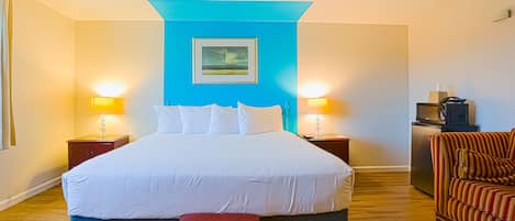 A hotel room with a large bed, two bedside lamps, a small table with a lamp, a television, and a striped armchair.