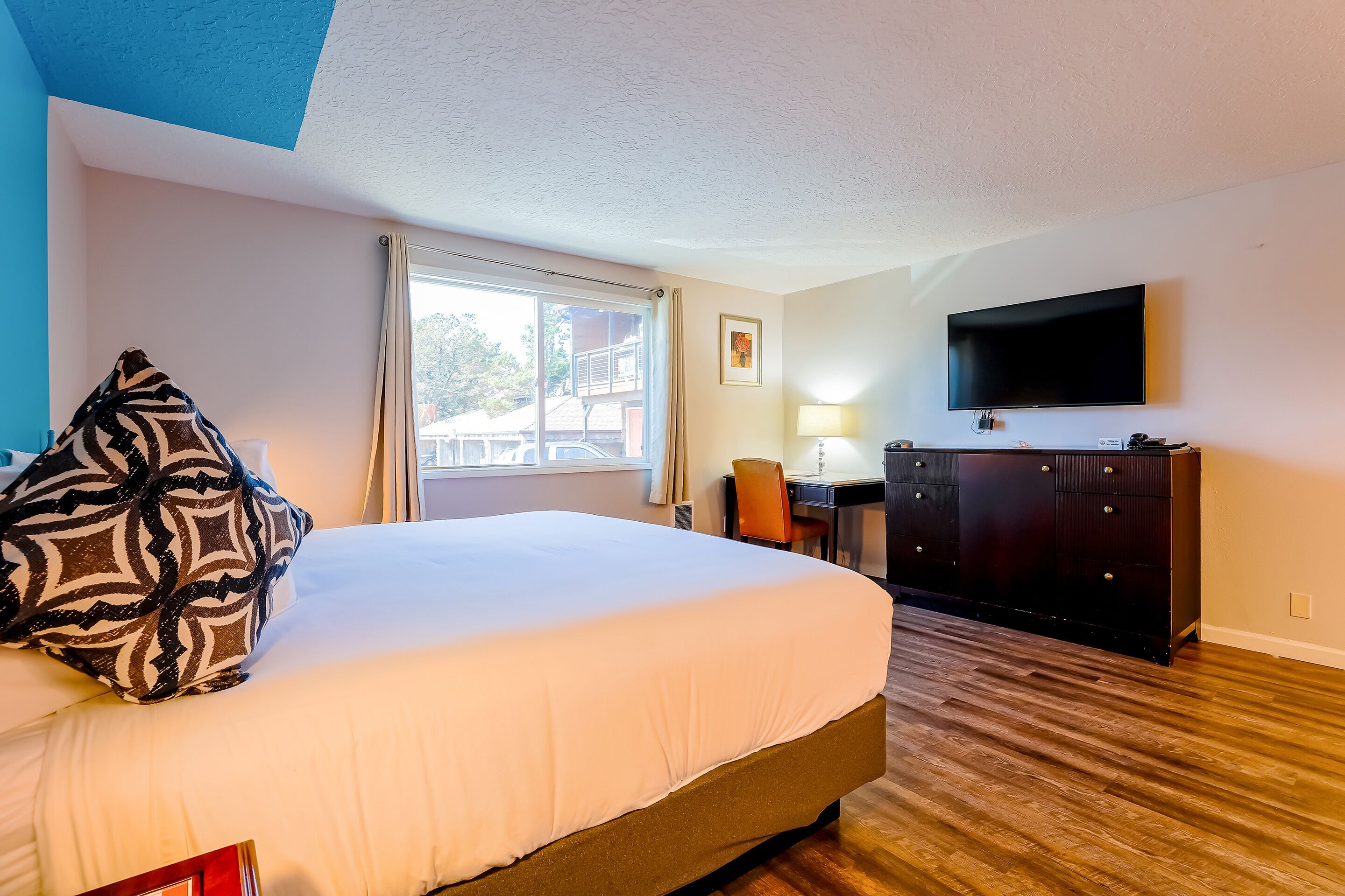 A hotel room with a large bed, a desk, a TV, and a window with curtains.