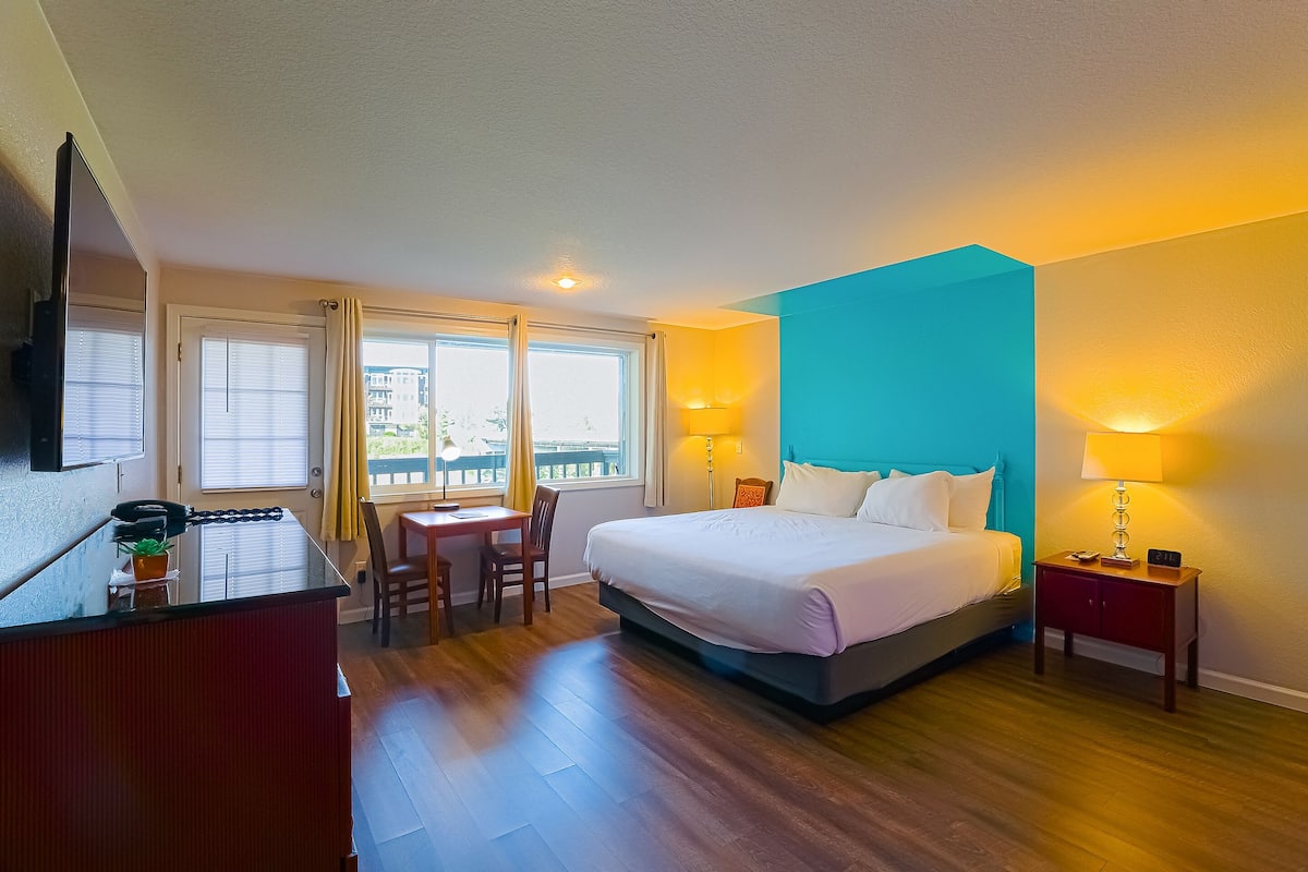 A hotel room with a bed, bedside table, desk, chair, and a TV.
