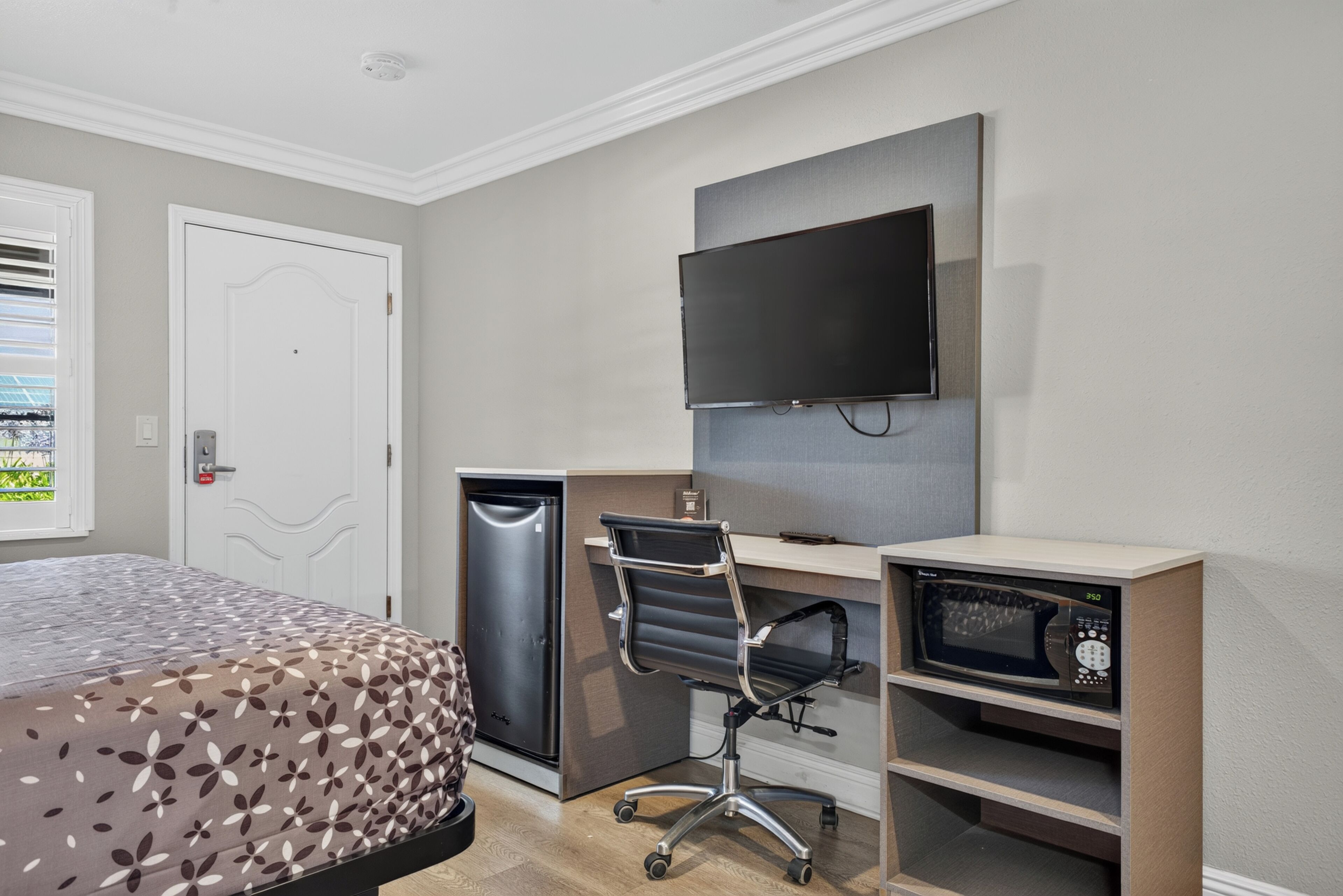 A hotel room with a bed, a desk, a chair, a television, and a microwave.