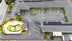 Vista aérea de un estacionamiento con espacios demarcados, un área ajardinada con diseño circular y un edificio con techo inclinado.