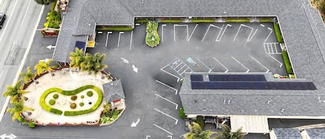 An aerial view of a parking lot with marked spaces, a landscaped area with a circular design, and a building with a sloped roof.