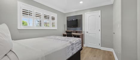 Un dormitorio con cama, televisor, escritorio y ventana con persianas.