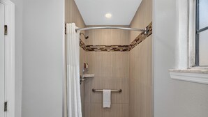 Baño con ducha, suelo de baldosas y un perchero.