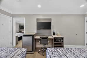 A hotel room with two beds, a desk with a computer, a microwave, and a mini fridge.