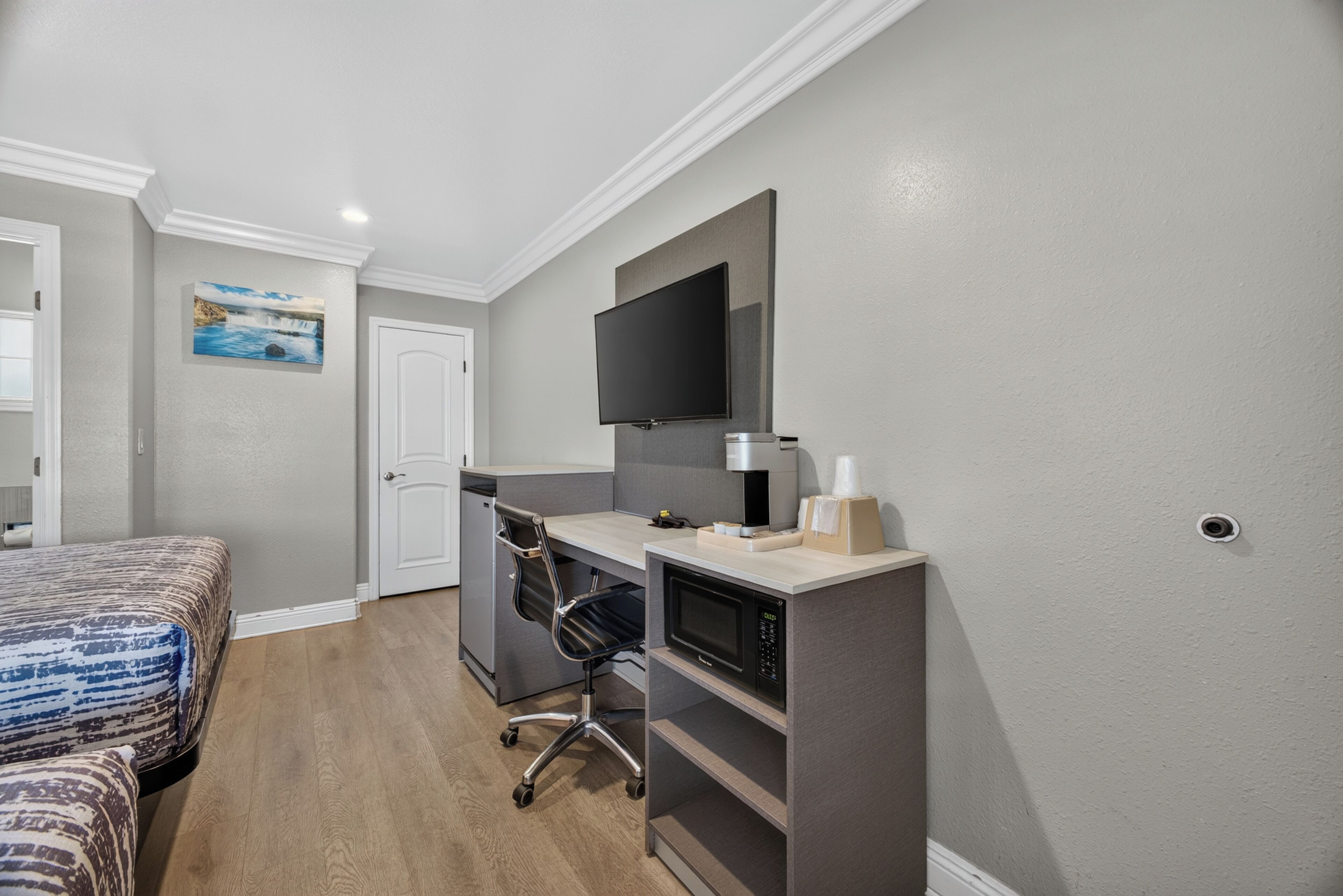 A hotel room with a bed, a desk with a computer, a flat-screen TV, and a microwave.