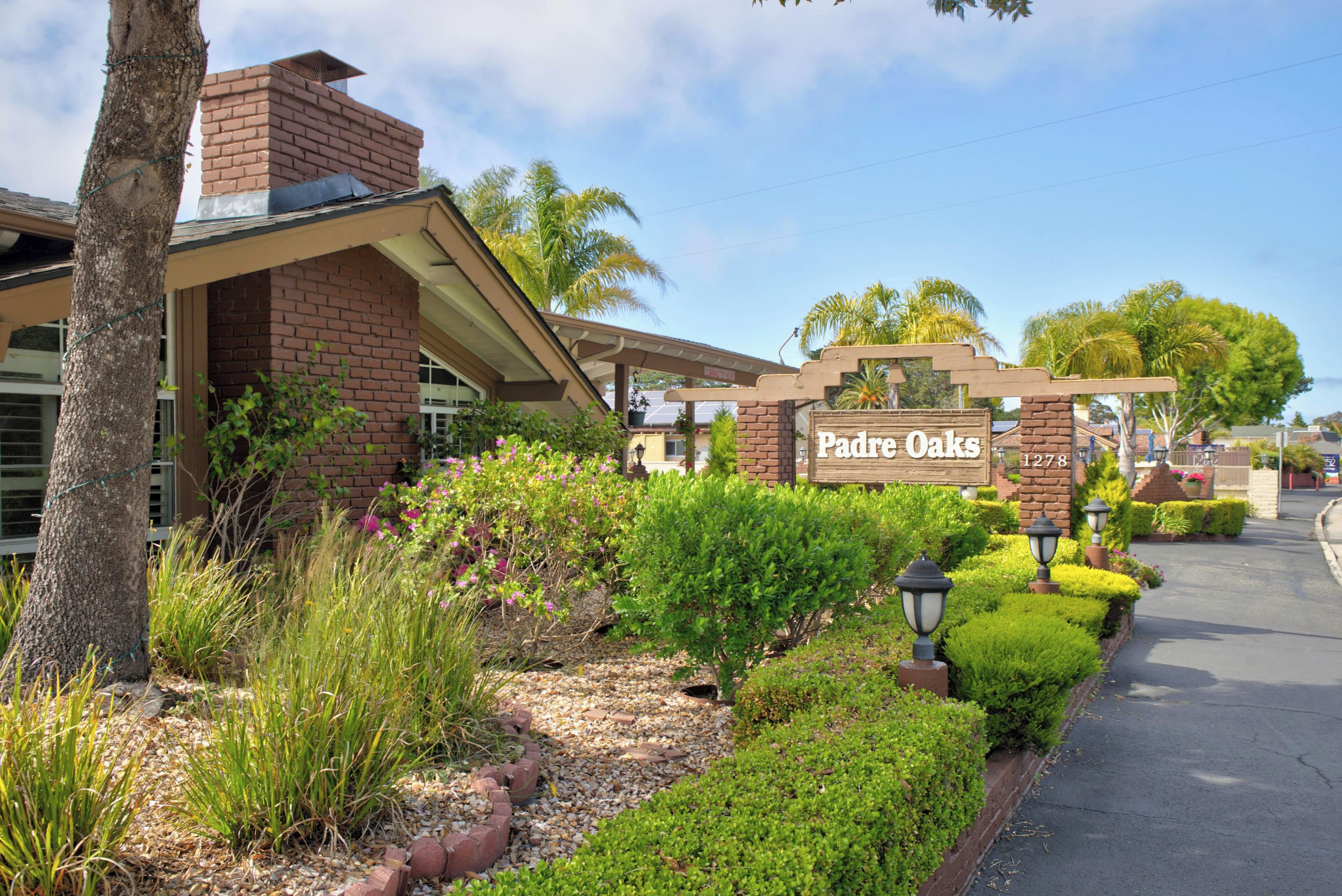 A hotel entrance with a brick facade, a sign reading 'Padre Oaks,' and well-maintained landscaping.