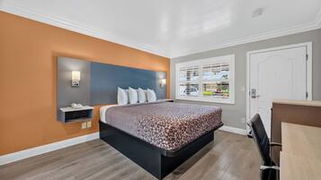 A hotel room with a bed, a desk, a chair, a window with blinds, and a wall-mounted phone.