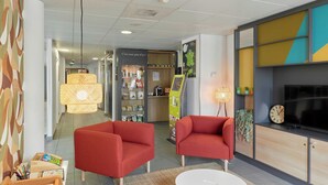 A modern lobby with red armchairs, a white coffee table, and a reception desk with a digital kiosk.