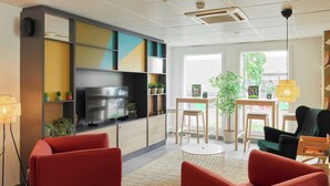 A modern living room with a flat-screen TV, red sofas, a small round table, and a bookshelf with colorful panels.