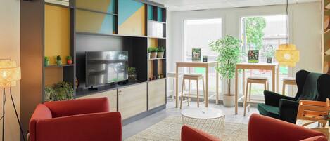 A modern living room with a flat-screen TV, red sofas, a small round table, and a bookshelf with colorful panels.