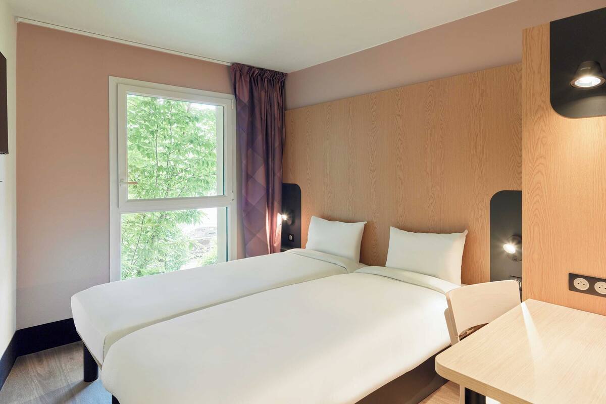 A hotel room with a large bed, a small table, and a window with curtains.