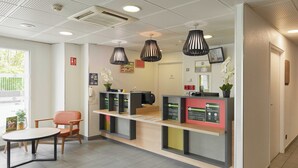 A reception area with a counter, chairs, and a table. There are hanging lights and a door in the background.