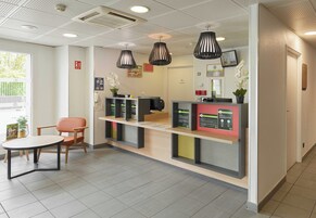 Zona de recepción con mostrador, sillas y una mesa. Se observan luces colgantes y una puerta al fondo.
