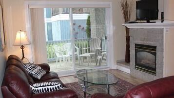 A living room with a glass coffee table, leather sofas, a fireplace, and a TV on a mantel.