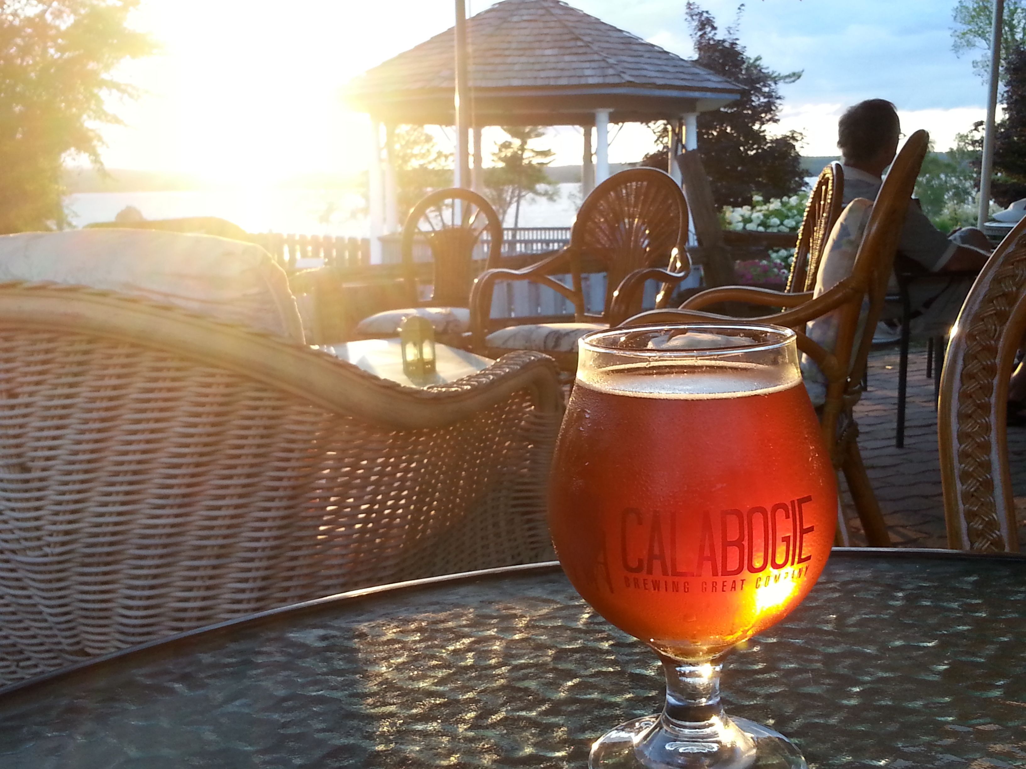 Ein Bierglas auf einem Tisch mit Korbstühlen und einem Pavillon im Hintergrund.